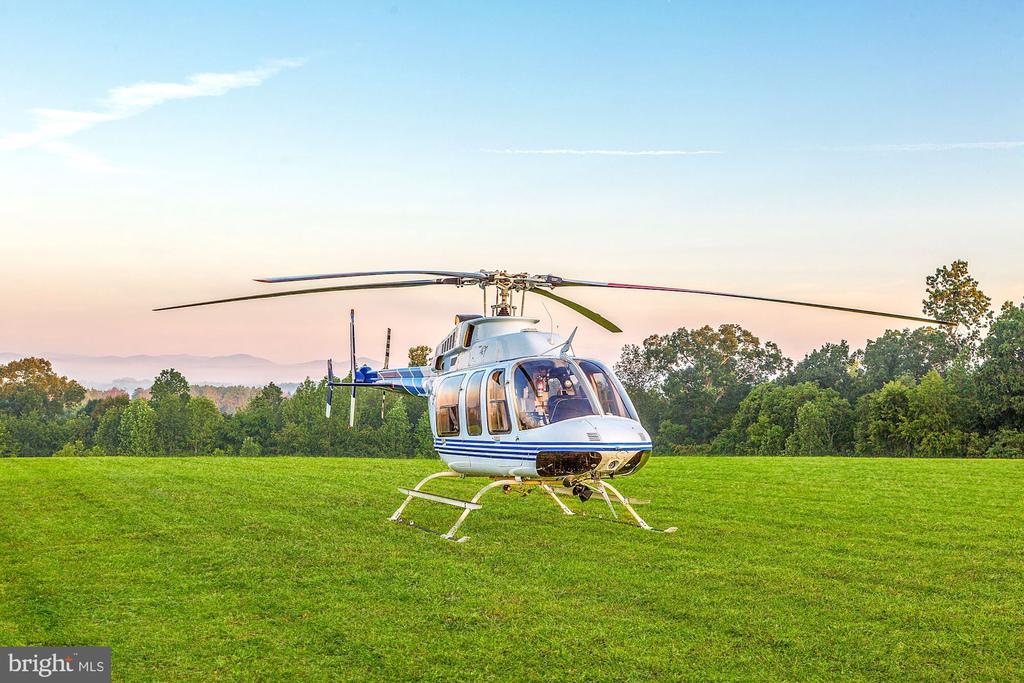 Helicopter parked on a grassy field, with trees and distant mountain ridges at sunset.