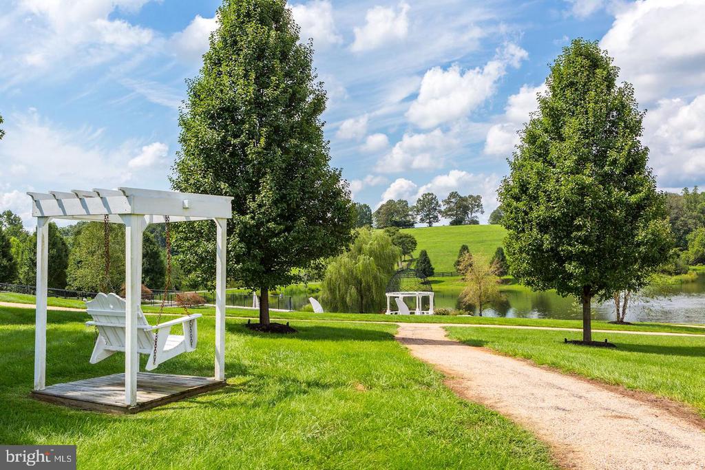 Landscaped grounds with a white pergola swing, curving path, and pond.