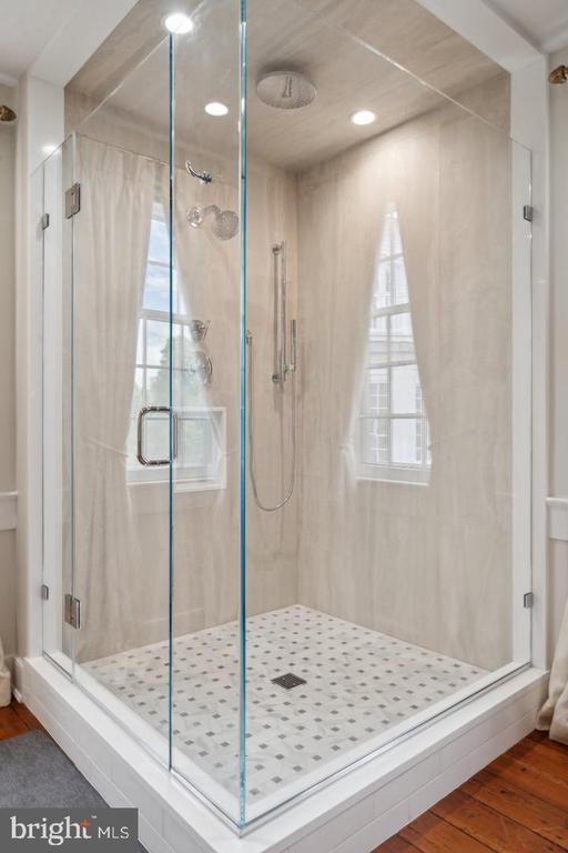 Walk-in glass shower with marble-look walls, rainfall showerhead, and patterned tile floor.