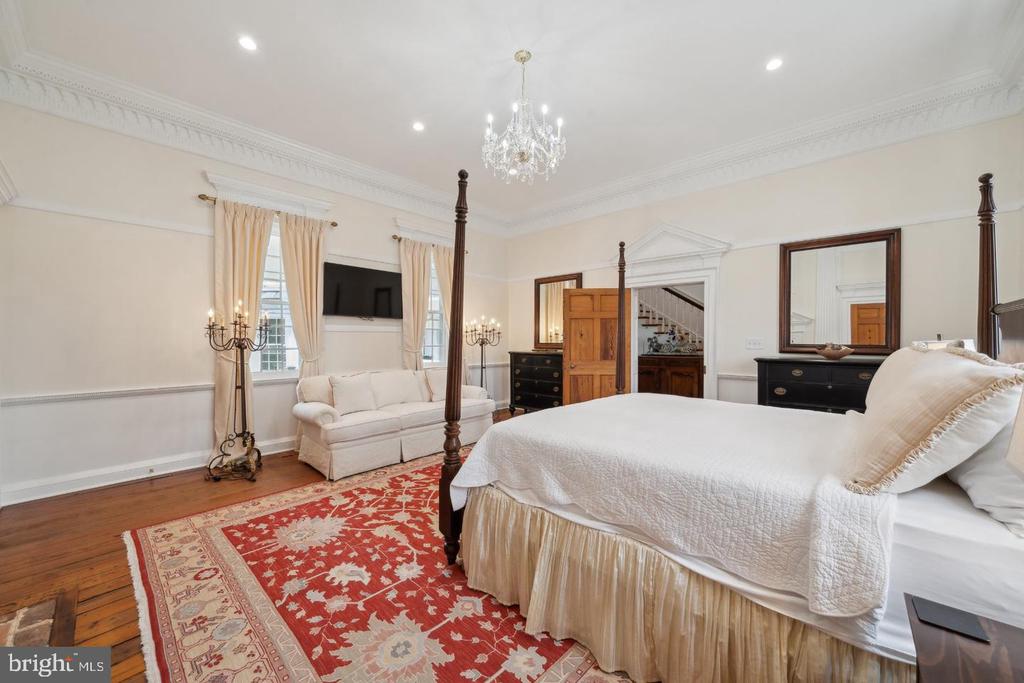 Bedroom with a four-poster bed, red patterned rug, white sofa, and crystal chandelier.