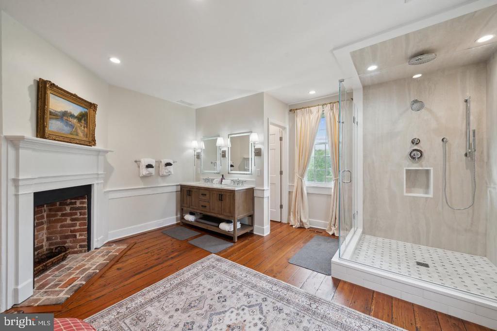 Spacious bathroom with a glass shower, wood vanity, brick fireplace, and hardwood floors.
