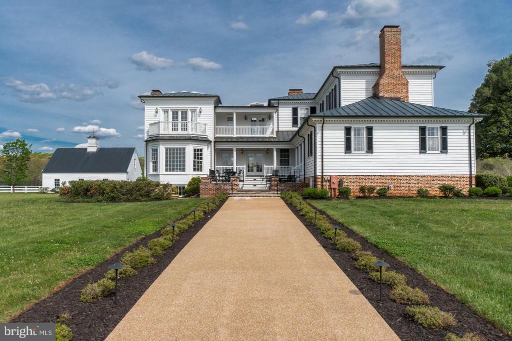 White two-story house with brick lower walls, black shutters, and a wide walkway to the entrance.