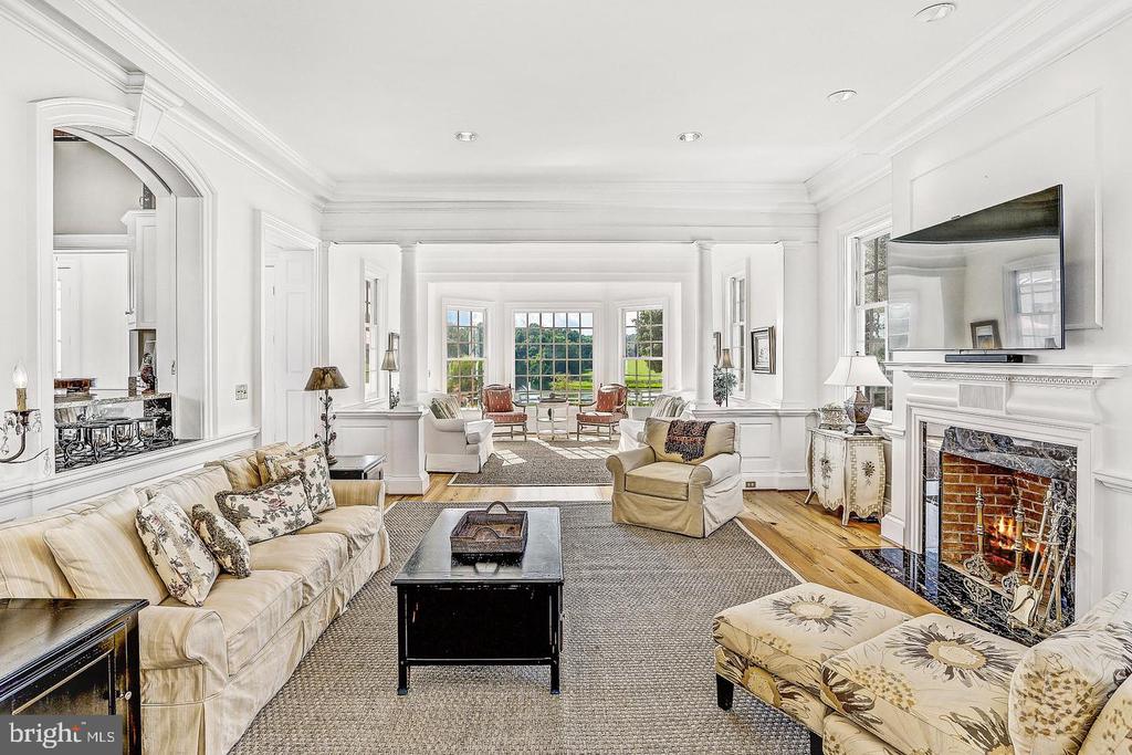 Living room with white paneling, a fireplace, mounted television, and large windows overlooking a lawn.
