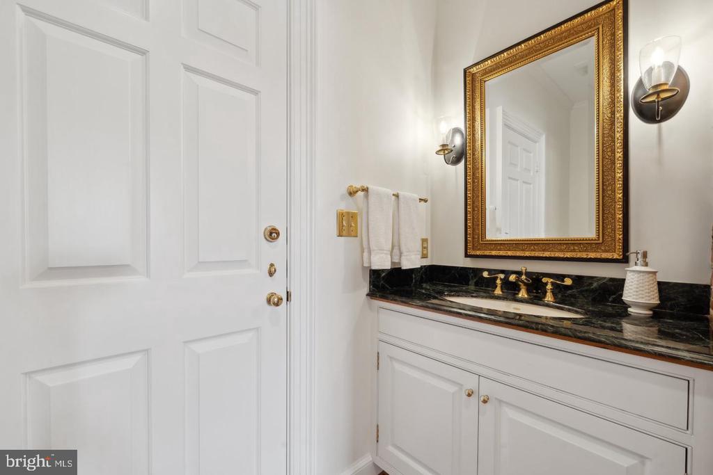 Bathroom vanity with black marble countertop, brass fixtures, and an ornate gold-framed mirror.