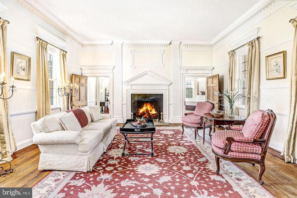 Formal living room with a lit fireplace, ornate white molding, and red patterned seating.