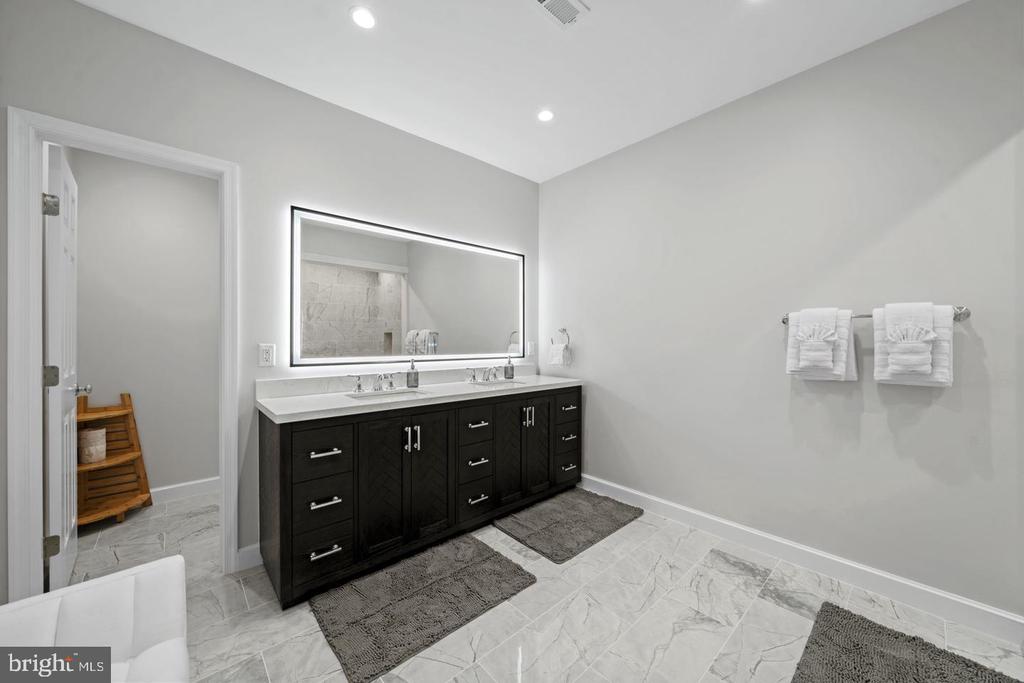 Bathroom with a dark double vanity, illuminated mirror, and gray tile floors.