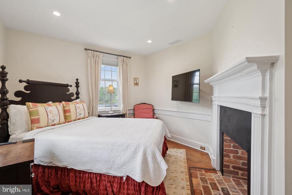 Bedroom with a four-poster bed, white mantel, and brick fireplace.