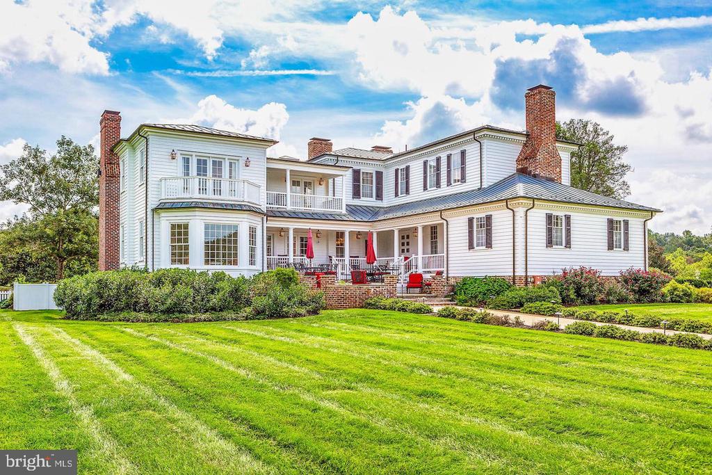 Large white house with brick chimneys, wraparound porches, and a broad green lawn.