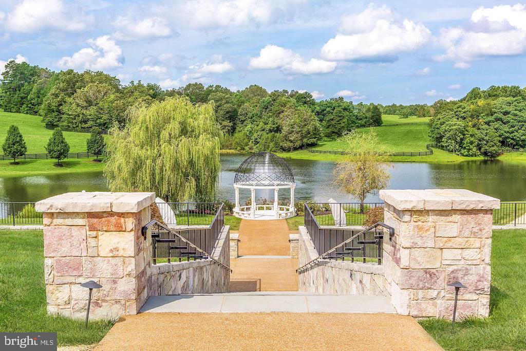Stone stairway descends to a white gazebo beside a pond on landscaped grounds.