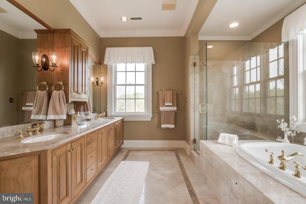 Bathroom with a long wood double vanity, glass shower, and built-in soaking tub beside large windows.