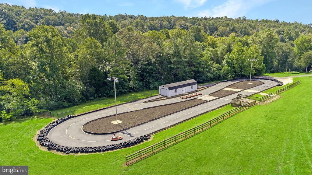 Go-kart track with tire barriers and a small building, surrounded by grass and woods.