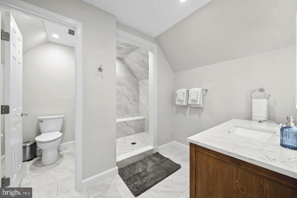 Bathroom with marble-tile shower, wood vanity, and separate toilet alcove.
