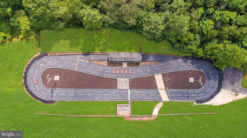 Paved oval track with tire barriers, landscaped center, and surrounding green lawn.