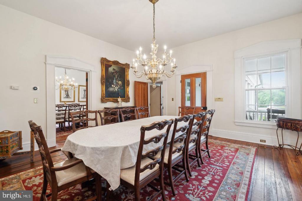 Formal dining room with a crystal chandelier, carved wooden chairs, hardwood floors, and red patterned rugs.