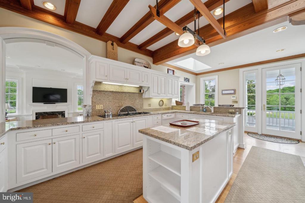 White kitchen with granite counters, a large island, exposed wood beams, and balcony doors.