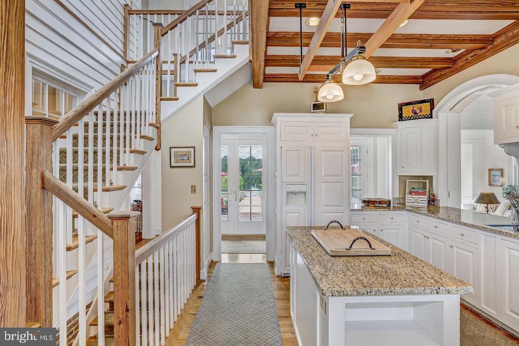 Kitchen with granite island and white cabinetry beside a staircase with wood handrails and exposed ceiling beams.