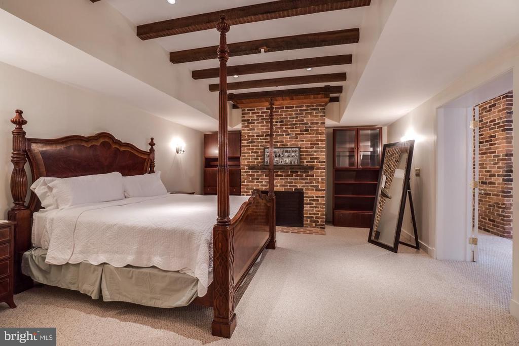 Bedroom with a carved four-poster bed, exposed ceiling beams, and a brick fireplace wall.