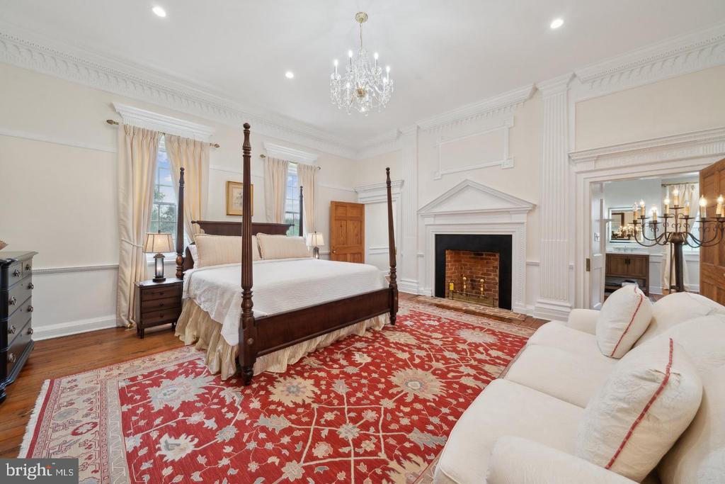 Furnished bedroom with a four-poster bed, ornate red rug, and white fireplace.
