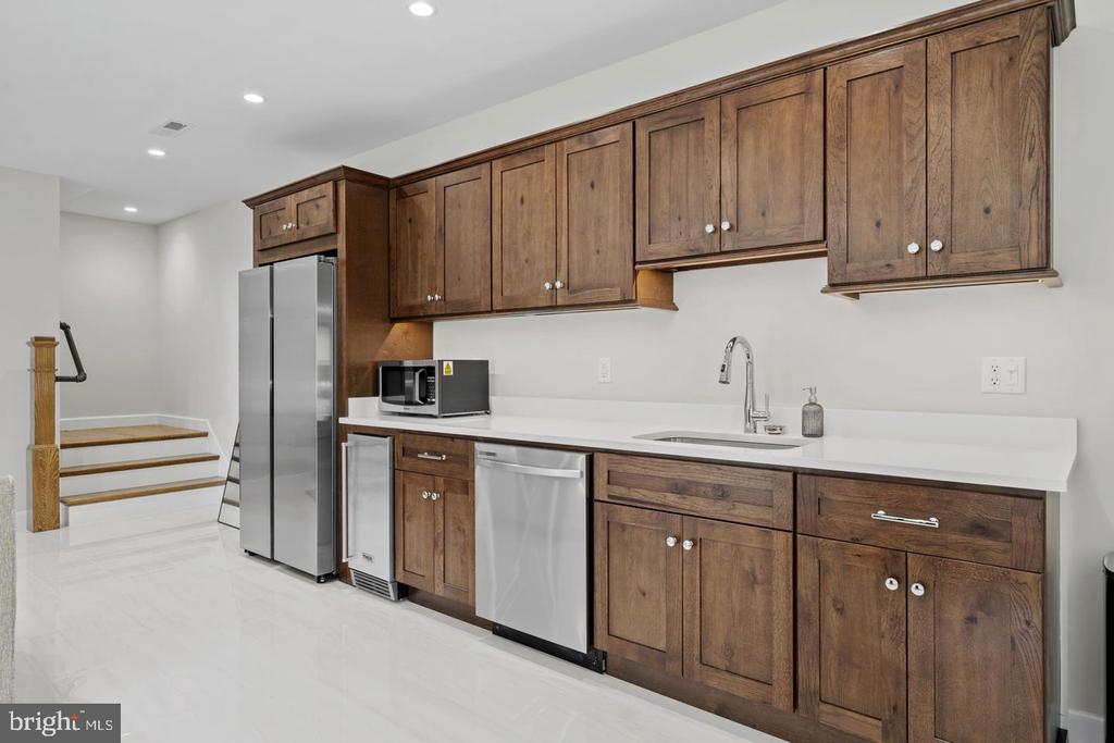 Kitchen with dark wood cabinets, white countertops, stainless steel appliances, and stairs beside the refrigerator.