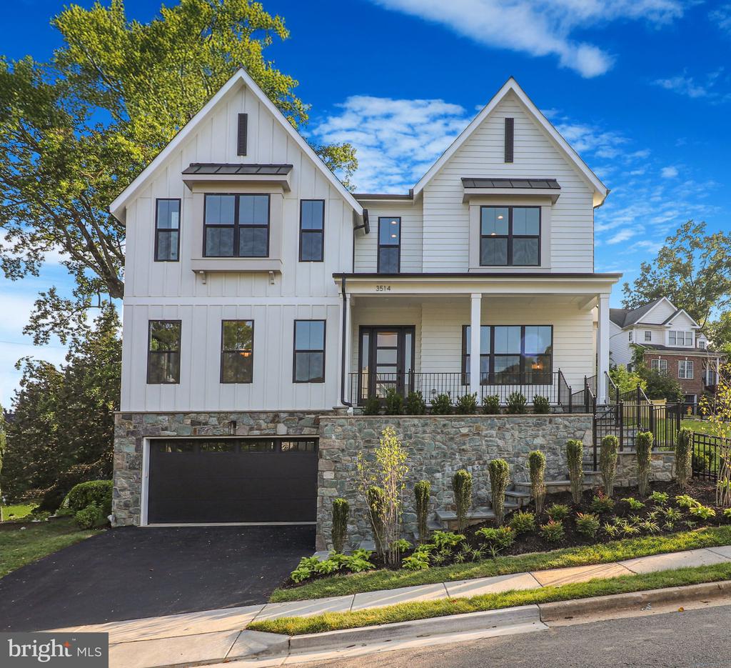 White two-story house with twin gables, a covered porch, and a stone foundation above an attached garage.