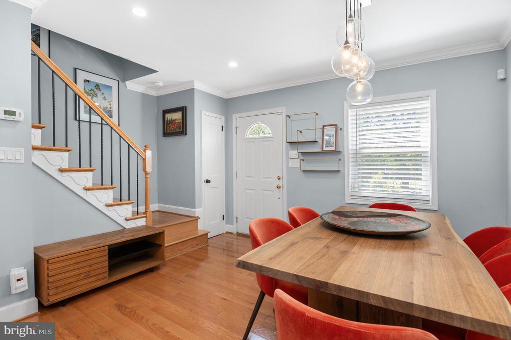 Dining room with a large wooden table and red chairs beside a staircase and front entry.