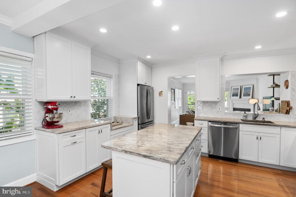 Bright white kitchen with a large stone island, stainless steel appliances, and hardwood floors.