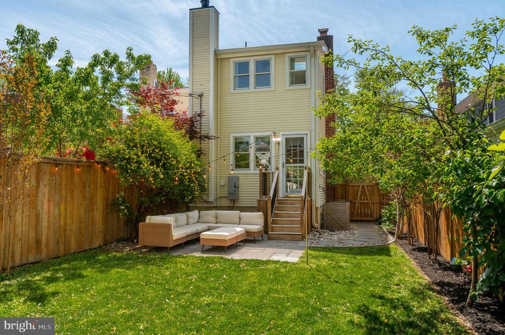 Rear of a light-yellow house with a fenced lawn, patio seating, and steps to glass doors.