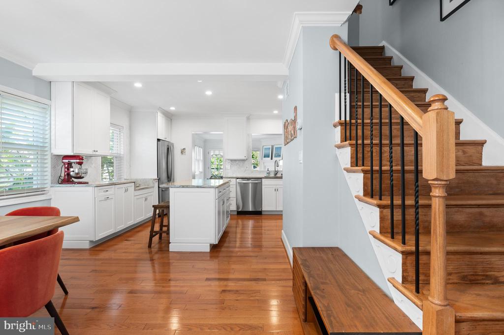 Bright kitchen with white cabinetry and island beside a hardwood staircase with black balusters.