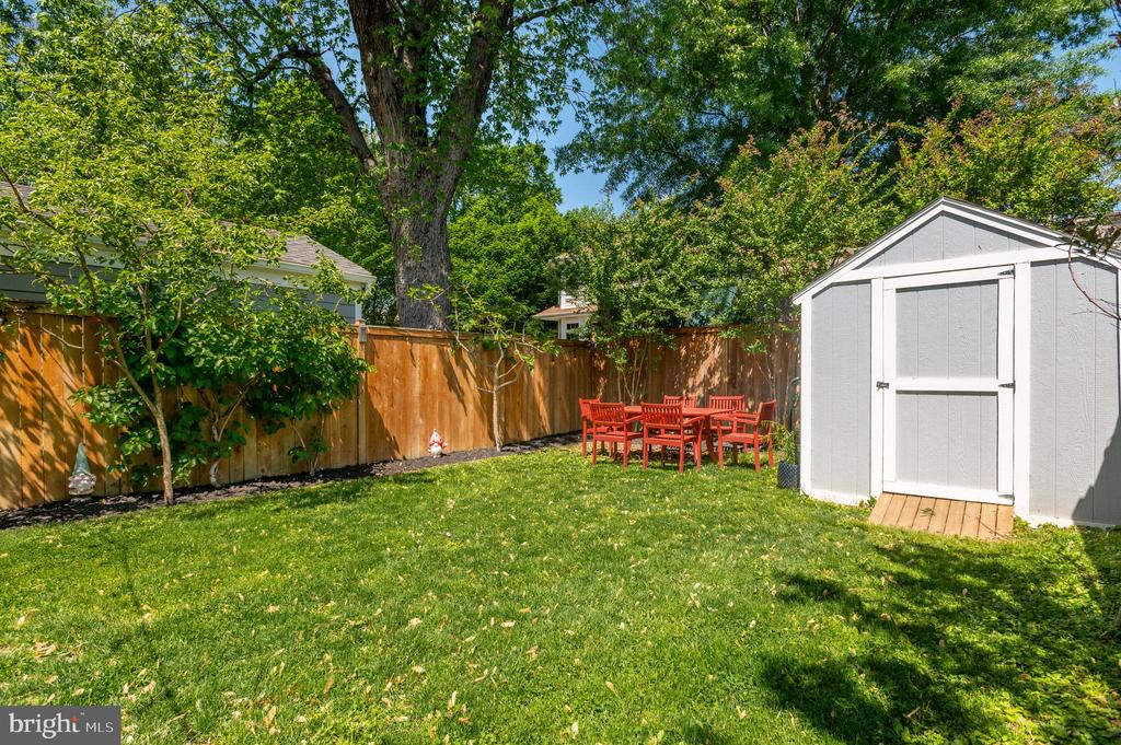 Fenced backyard with a broad lawn, gray storage shed, and red outdoor dining set.