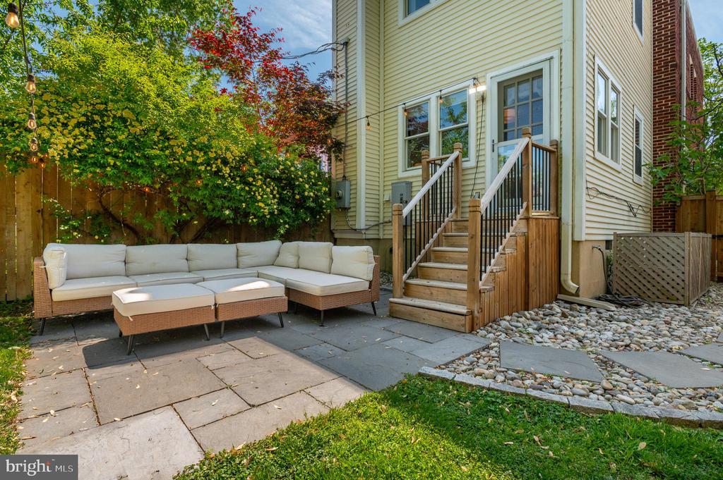 Backyard patio with a white sectional, stone paving, and steps to the house.