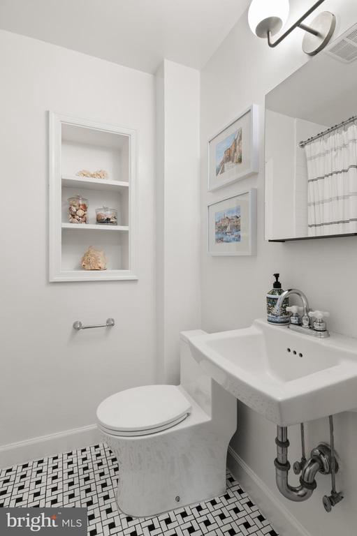 White bathroom with a console sink, recessed shelves, and black-and-white mosaic tile floor.
