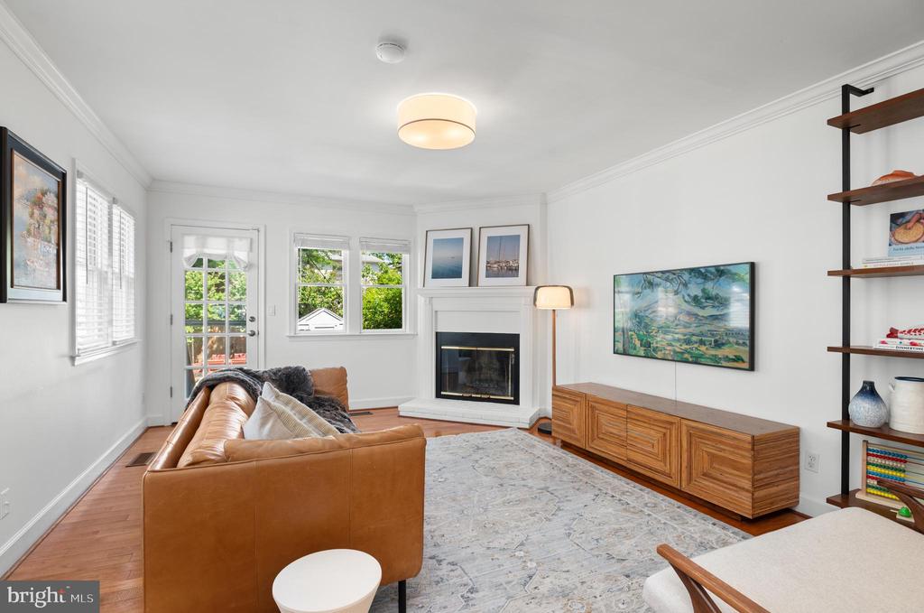 Living room with a fireplace, tan leather sofa, patterned rug, and wood media console.