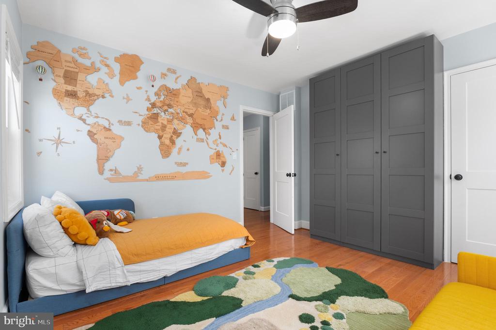Bedroom with a wooden world map wall feature, gray built-in wardrobes, and a blue bed with a mustard coverlet.