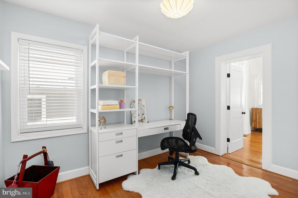 Home office with built-in white shelving, a black chair, and hardwood floors.