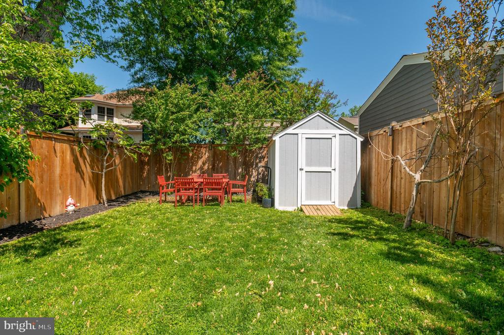 Fenced backyard with a green lawn, white shed, and red outdoor dining set.
