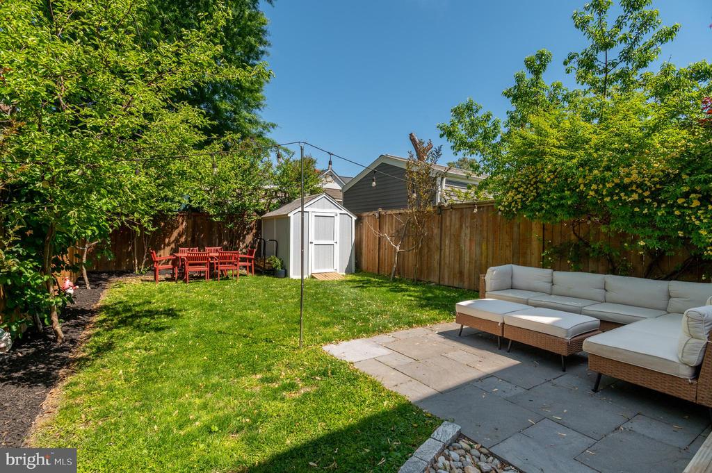 Fenced backyard with a stone patio, outdoor sectional, lawn, and white storage shed.