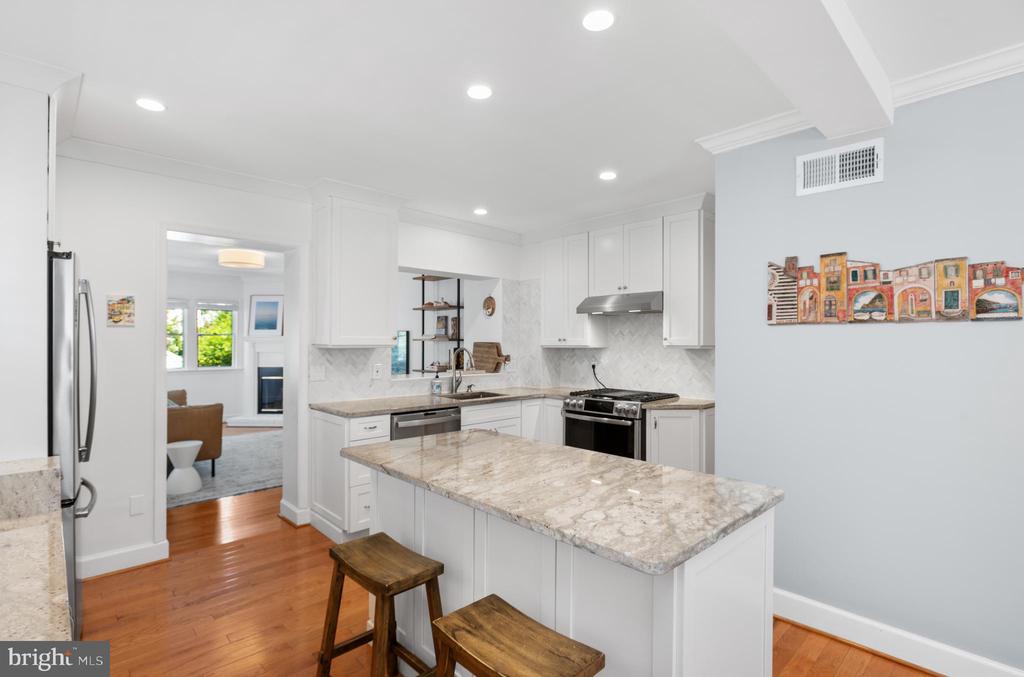 Kitchen with white cabinets, a large stone island, stainless steel appliances, and an open doorway to a sitting room.