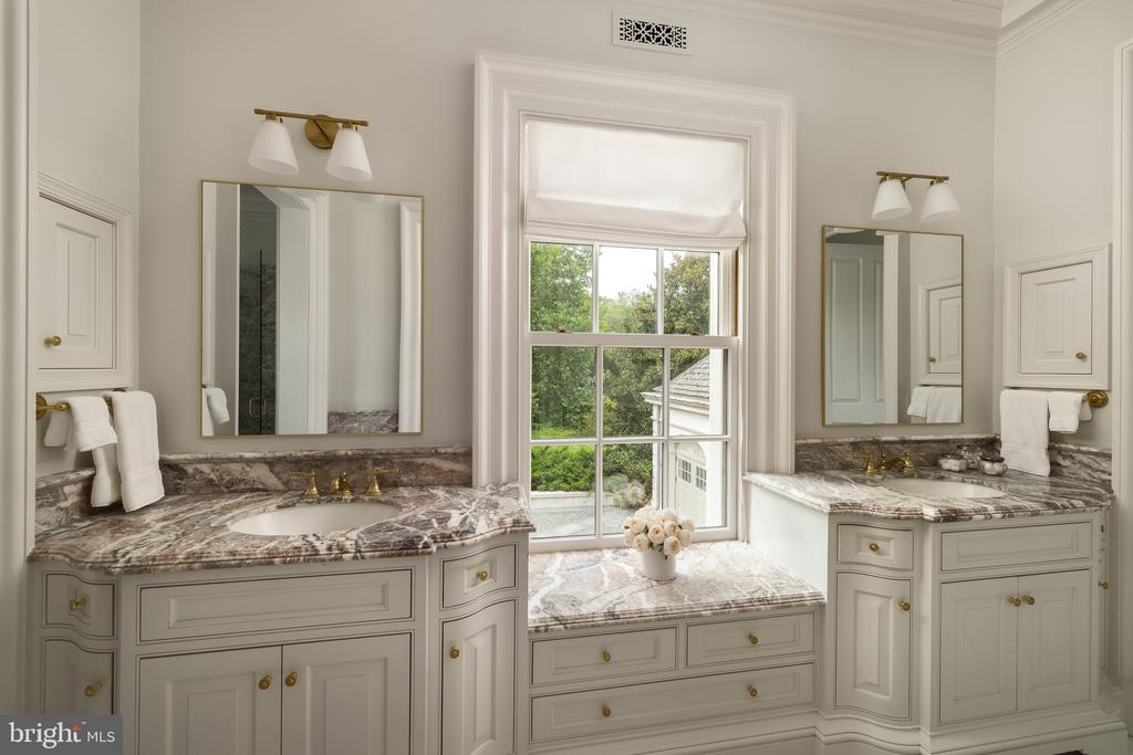 Bathroom with dual marble-topped vanities and a large window above a built-in seat.