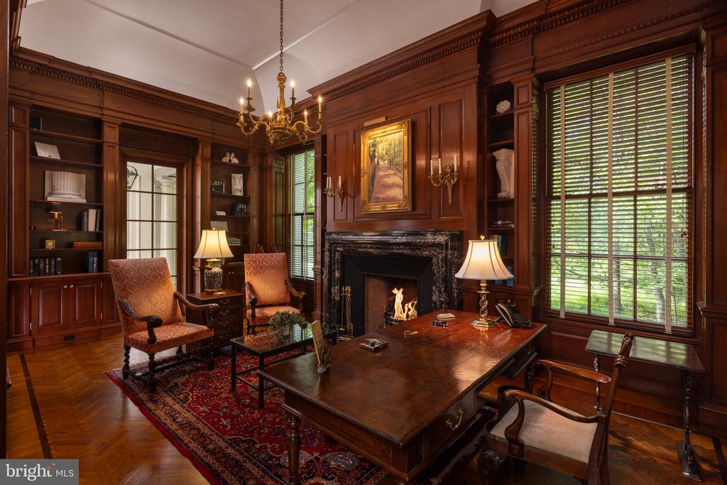 Wood-paneled study with built-in bookshelves, a large desk, and a fireplace.