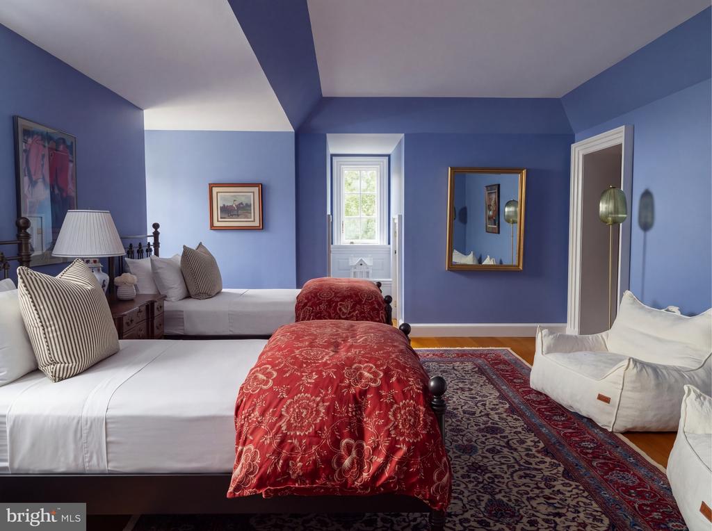 Bedroom with twin beds, red patterned quilts, deep blue walls, and a patterned rug.