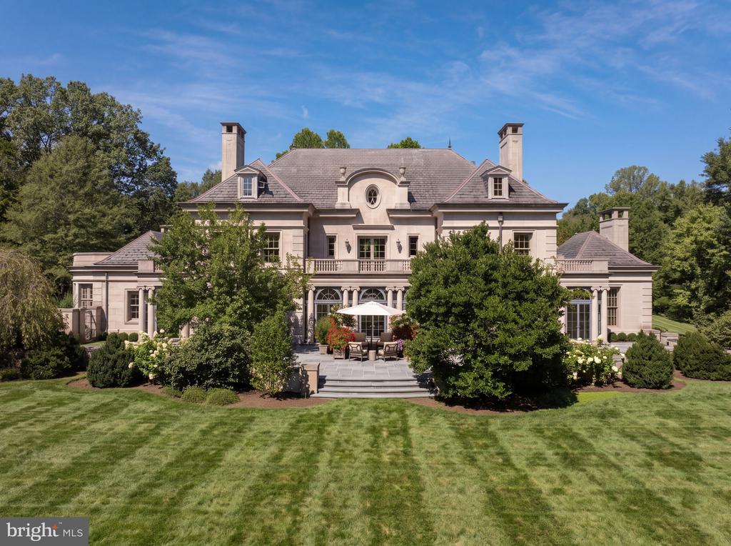 Stone mansion with a central patio and umbrella, landscaped gardens, and a broad lawn.