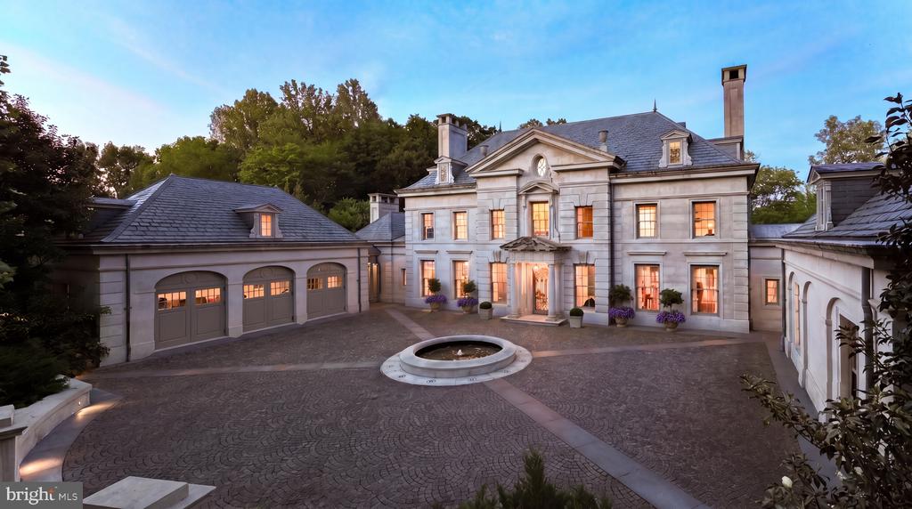 Stone mansion with illuminated windows, attached garage wings, and a circular fountain in the courtyard.