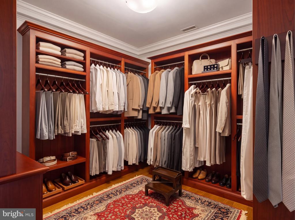 Walk-in closet with rich wood built-ins, neatly arranged clothing, shoes, and a patterned rug.