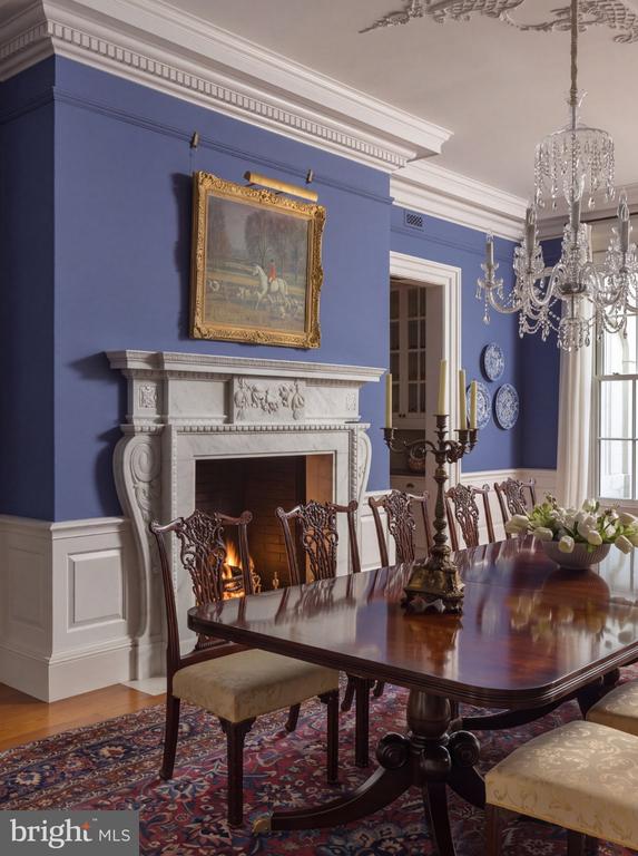 Formal dining room with a polished table, carved chairs, and a lit fireplace.