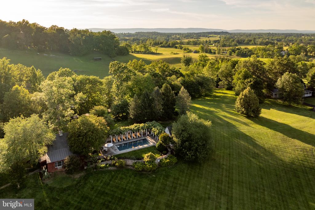 Aerial view of a country property with a swimming pool, broad lawn, and rolling fields.