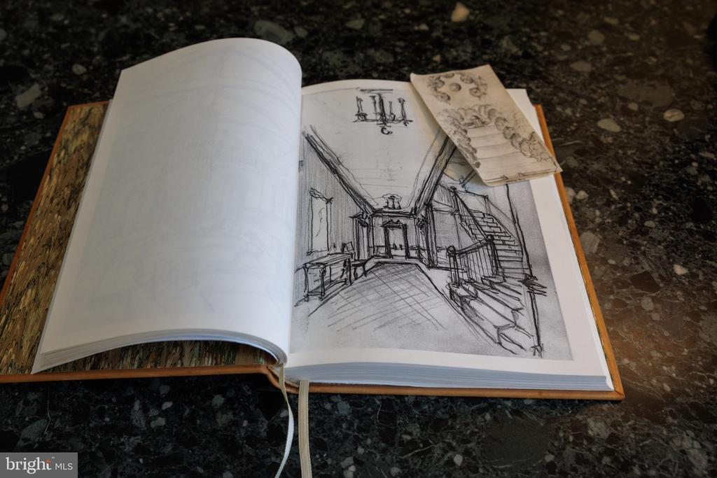 Open sketchbook showing a pencil drawing of a foyer and staircase on a dark stone countertop.