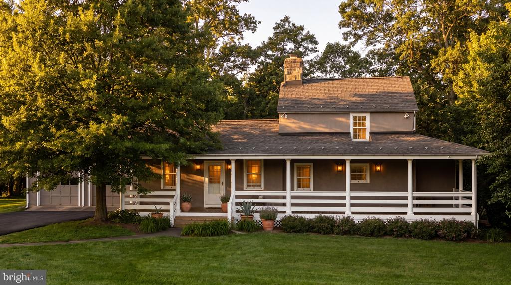 Gray two-story house with a long white-railed porch and attached garage among mature trees.