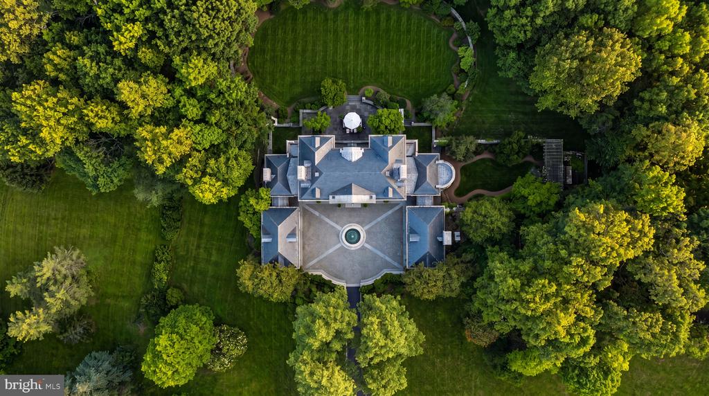 Aerial view of a large estate house with a circular fountain courtyard, lawns, and mature trees.