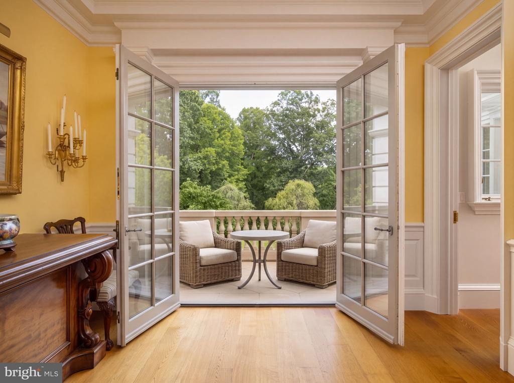 Interior with open French doors leading to a terrace with wicker seating and leafy views.
