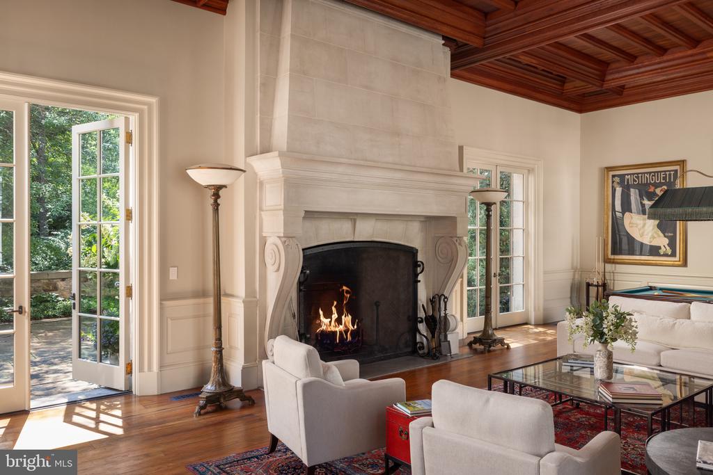 Living room with a grand white fireplace, coffered wood ceiling, and French doors to the garden.